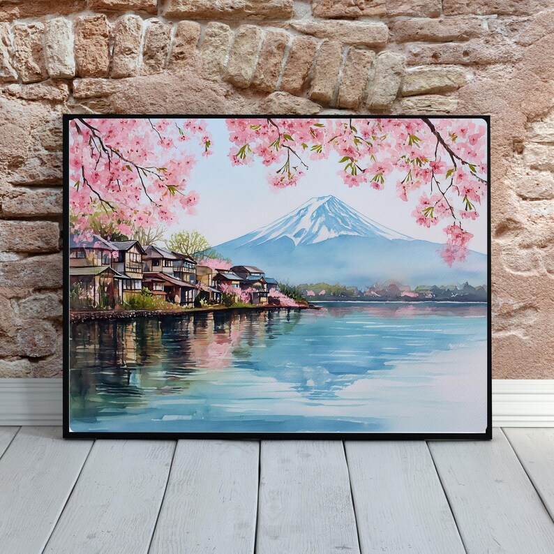 Peut inclure: Peinture &agrave; l'aquarelle d'un paysage japonais avec le Mont Fuji, un lac et des maisons traditionnelles. Des fleurs de cerisier roses encadrent le haut de l'image. L'&oelig;uvre est encadr&eacute;e en noir, contre un mur de briques et un sol en bois blanc.