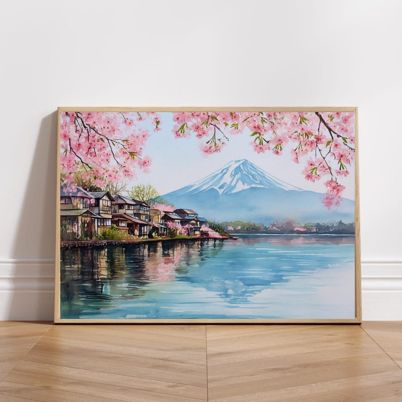 Peut inclure: Peinture &agrave; l'aquarelle d'un paysage japonais avec le Mont Fuji, un lac et des maisons traditionnelles. Des fleurs de cerisier roses encadrent la sc&egrave;ne. L'&oelig;uvre est encadr&eacute;e dans un cadre en bois clair.