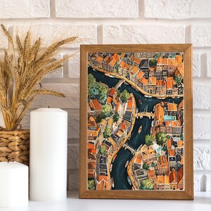 May include: An aerial view of a city with narrow canals and colourful buildings. The buildings are mostly brick and have red tile roofs. The canals are lined with trees and there are boats on the water.