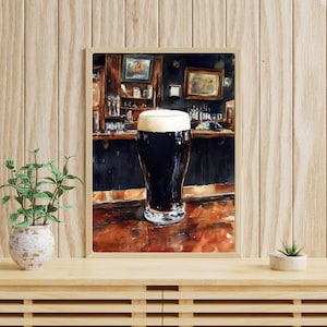 May include: Watercolor painting of a pint of dark stout beer with a thick, creamy head, set in a traditional pub scene. The artwork features a wooden bar, bottles, and framed pictures, creating a cozy atmosphere. The painting is in a wooden frame.