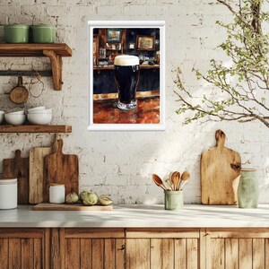 May include: A framed watercolor painting of a pint of dark beer with a thick, creamy head, set on a bar. The bar is dark with a wooden surface, and the background shows a pub interior.