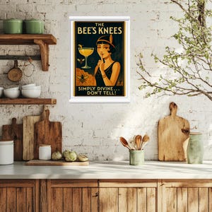 May include: A framed vintage-style poster with the text "The Bee's Knees" and a woman in a flapper dress. The poster features a cocktail glass, a bee, and the words "Simply Divine... Don't Tell!" in a kitchen setting.