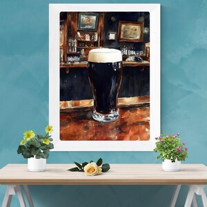 May include: Watercolor painting of a pint of dark beer with a thick, creamy head, set against a bar backdrop. The bar features dark wood and framed pictures. The artwork is framed in a white border.