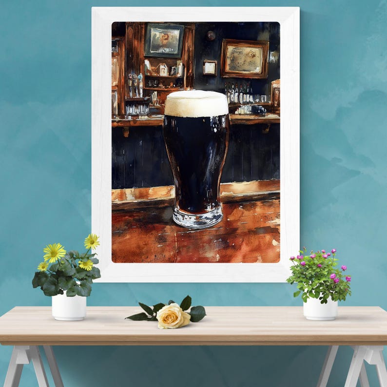 May include: Watercolor painting of a pint of dark beer with a thick, creamy head, set against a bar backdrop. The bar features dark wood and framed pictures. The artwork is framed in a white border.