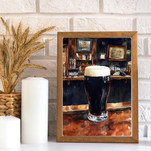 May include: A framed print of a pint of dark beer with a thick, creamy head, set in a pub scene. The artwork features a wooden bar, dark walls, and framed pictures. The print is in a wooden frame.