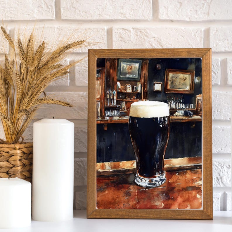 May include: A framed print of a pint of dark beer with a thick, creamy head, set in a pub scene. The artwork features a wooden bar, dark walls, and framed pictures. The print is in a wooden frame.
