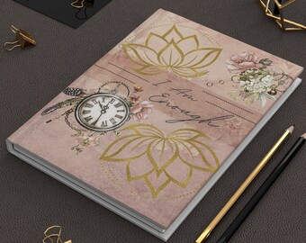 May include: A pink and gold journal with a floral design and the text "I Am Enough". The journal has a white cover and a gold clock face with roman numerals.