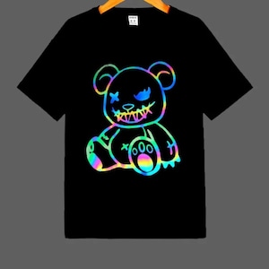 May include: Black t-shirt featuring a rainbow iridescent graphic of a cartoon teddy bear with stitches and a menacing grin.