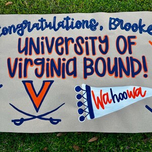 May include: A hand-painted sign on a tan background with the words "Congratulations, Brooke!" and "UNIVERSITY OF VIRGINIA BOUND!" in blue and orange. Includes the University of Virginia logo and "Wahoowa".