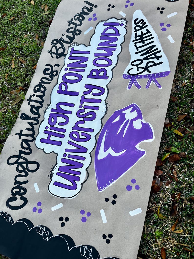 May include: A handmade banner with the words "Congratulations, Brixton! High Point University Bound!" in black and purple lettering. The banner also features a purple panther head and a white pennant with "Be Panthers" written on it.