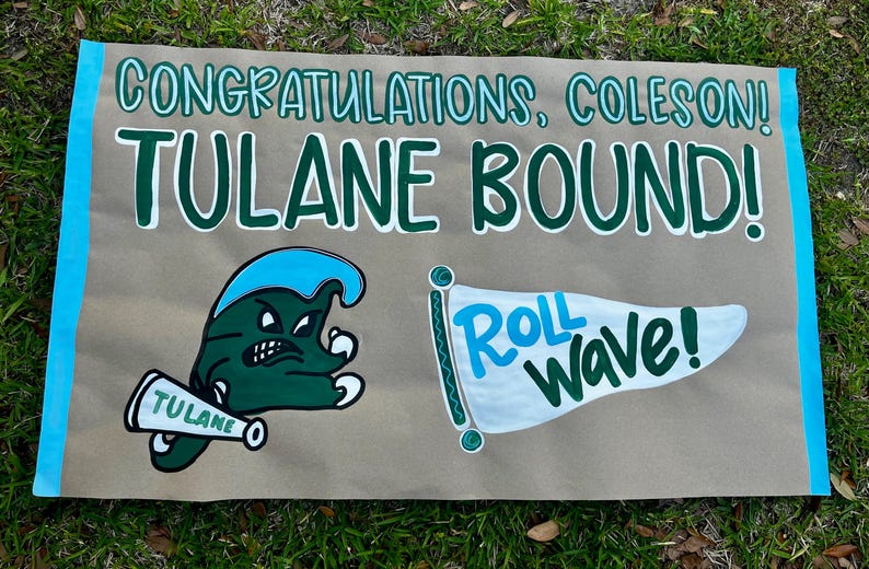 May include: A hand-painted sign on brown paper with blue borders and green text that reads "CONGRATULATIONS, COLESON! TULANE BOUND!" with a Tulane mascot and a flag that says "Roll Wave!"