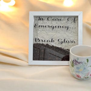 May include: White framed box with the text "In Case Of Emergency... Break Glass" and a clear glass panel filled with coffee beans.