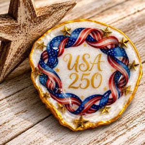 May include: A round, white, glittery resin coaster with a gold-painted edge, featuring a central red, white, and blue ribbon design forming a circle around the gold text USA 250, accented by small gold stars embedded along the perimeter.
