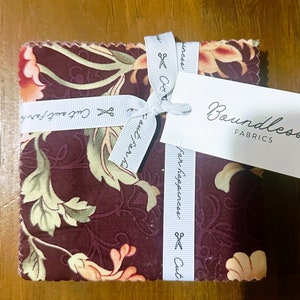 May include: A bundle of fabric squares with a floral pattern in shades of brown, green, and orange. The fabric is tied with a white ribbon with the text "Cut & Sew" and "Boundless Fabrics".