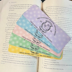 May include: A set of five colorful bookmarks with the text "I read books that hurt my feelings" printed on them. The bookmarks are decorated with a floral pattern and have a whimsical design.