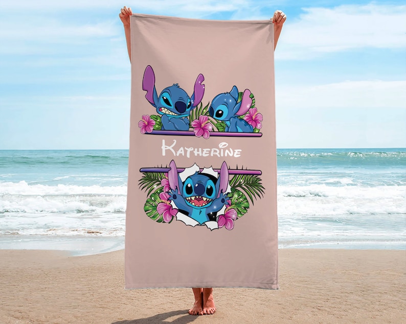 May include: A pink beach towel with a design featuring Stitch from Lilo & Stitch. The towel has a floral design and the name "Katherine" written on it.