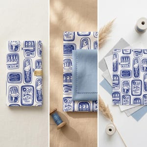 K&ouml;nnte beinhalten: Eine Sammlung von Stoffmustern und ein Notizbuch mit einem sich wiederholenden Muster aus blau-wei&szlig;en Sardinenb&uuml;chsen. Das Bild zeigt einen blauen Stoffmuster, Garnrollen und verschiedene Stoffmuster in Blau- und Graut&ouml;nen.