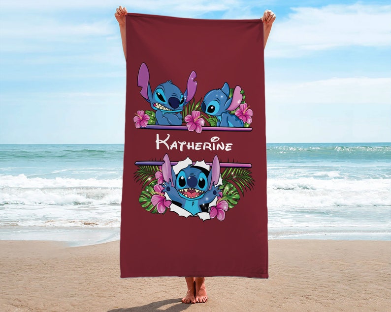 May include: A red beach towel with a personalized name "Katherine" and a cartoon image of Stitch from Lilo & Stitch. The Stitch image is surrounded by tropical flowers and leaves.