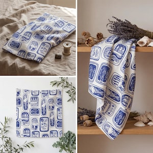 K&ouml;nnte beinhalten: Wei&szlig;-blaue K&uuml;chent&uuml;cher mit Sardinen-Dosen-Muster. Die T&uuml;cher sind aus einem weichen Stoff gefertigt und mit einem sich wiederholenden Muster aus blauen Sardinen-Dosen auf wei&szlig;em Grund verziert. Die T&uuml;cher sind gefaltet und in verschiedenen Umgebungen ausgestellt.
