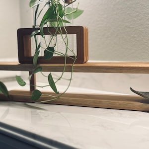 Könnte beinhalten: Ein Holzregal mit einem einzigartigen geschwungenen Design, das eine Topfpflanze, eine Kerze und ein dekoratives Blatt zeigt. Das Regal ist aus hellem Holz gefertigt und hat eine natürliche Oberfläche.