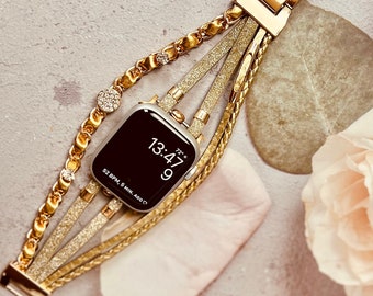 May include: A gold Apple Watch with a sparkly gold band and a white face displaying the time 13:47. The watch is surrounded by pink roses and eucalyptus leaves.