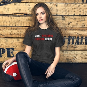 May include: A dark heather grey t-shirt with the text "MAKE DYSTOPIA FICTION AGAIN" in red and white lettering.