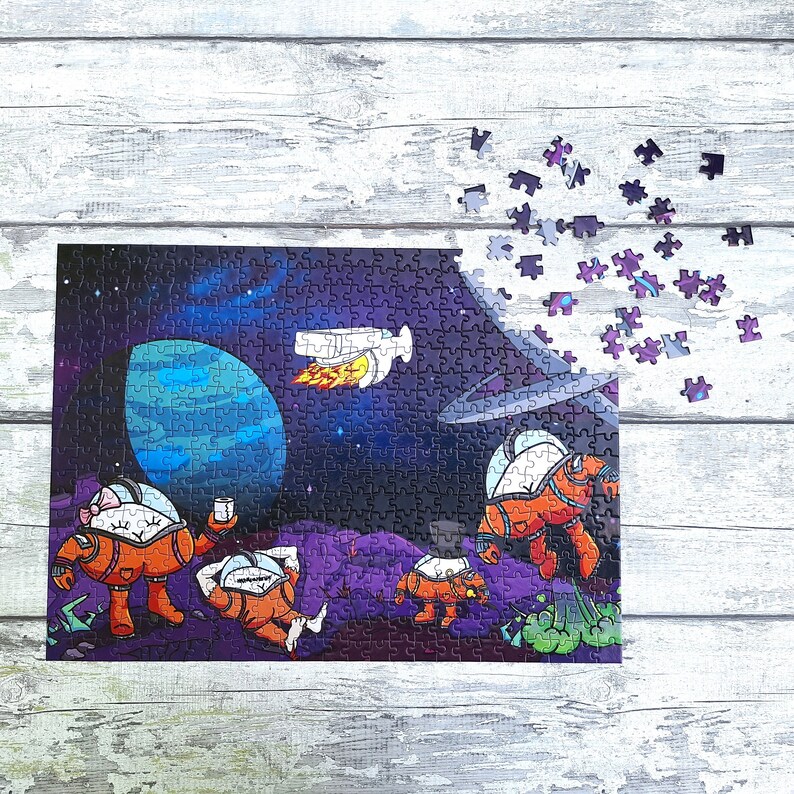 May include: A colorful jigsaw puzzle depicting a space scene with four astronauts in spacesuits, a planet, and a rocket ship. The puzzle pieces are scattered around the completed puzzle.