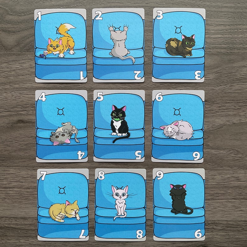 May include: Nine blue cards with white numbers and white outlines. Each card features a different cat illustration in a blue armchair. The cards are numbered 1 through 9.