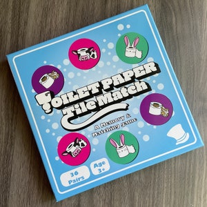 Può includere: Una scatola di gioco blu e bianca con il titolo "Toilet Paper Tile Match" e il testo "A Memory & Matching game". La scatola presenta illustrazioni di rotoli di carta igienica, conigli e mucche. La scatola è etichettata "36 Pairs" e "Age 3+".
