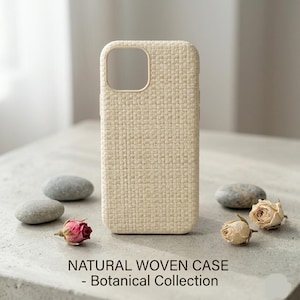 May include: A beige woven phone case with a rectangular shape and a camera aperture. The case is surrounded by small grey stones and dried roses. The text at the bottom reads "NATURAL WOVEN CASE - BOTANICAL COLLECTION."
