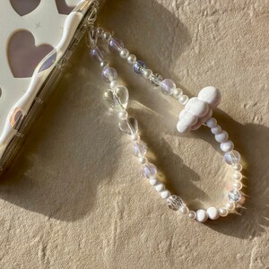May include: A white phone charm with a cloud charm and a beaded chain with white and clear beads.