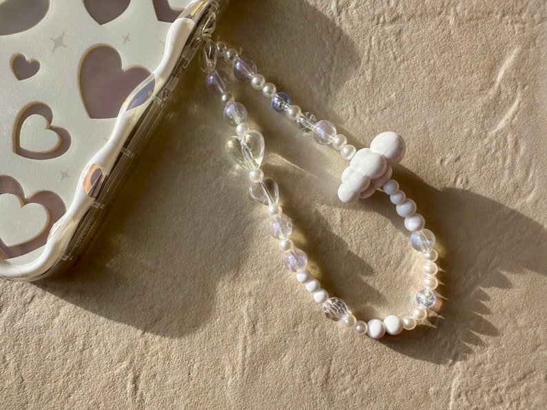 May include: A white phone charm with a cloud charm and a beaded chain with white and clear beads.