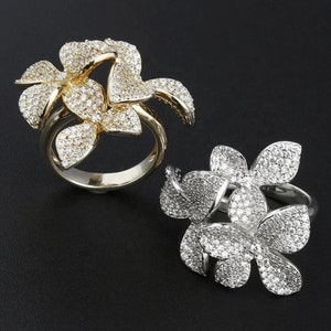 May include: Two flower-shaped rings with clear cubic zirconia stones. One ring is gold and the other is silver.