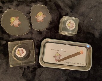 May include: A collection of smoking accessories featuring a cartoon owl design. Includes two resin coasters, a square ashtray, a small square container, and a metal rolling tray with the text "Don't Worry About a Thing, Everything Will Be Alright."