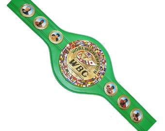 May include: Green and gold World Boxing Council (WBC) championship belt with a circular center plate featuring the WBC logo and flags of various countries. The belt has a green strap with gold accents and features photos of boxers.