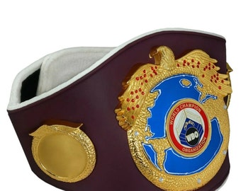 May include: A gold and blue boxing championship belt with a large eagle and a globe design. The belt has the words "World Champion" and "WBO Organization" on it.