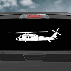 May include: A white helicopter decal is displayed on the rear window of a black pickup truck. The helicopter is a side profile with detailed features, including the rotor blades and tail. The background is a cloudy sky.
