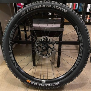 May include: A black bicycle wheel with a black tyre and a silver rim. The tyre has the text "EDDY CURRENT" printed on it. The rim has the text "SCHWALBE" printed on it.