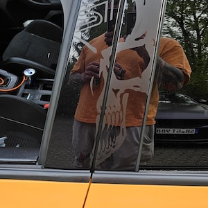 May include: A yellow car with black window trim and a skull decal on the rear window. The decal is a white outline of a skull with the word "STI" above it.