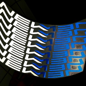 Peut inclure: Une feuille incurvée avec des motifs géométriques répétitifs en blanc et bleu. Les motifs blancs sont en zigzag, les bleus sont rectangulaires. La feuille est réfléchissante, sur fond sombre. Design graphique.