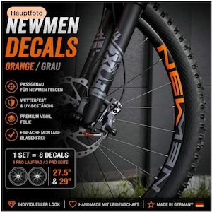 May include: A set of orange and gray vinyl decals for bicycle rims, featuring the text NEWMEN. The set includes 8 decals for 27.5-inch and 29-inch wheels. The image shows the decals applied to a black mountain bike wheel with a disc brake system.