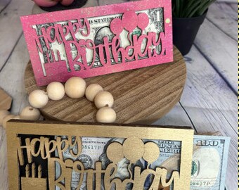 May include: Two wooden card holders with the words "Happy Birthday" in gold and pink glitter. The holders have a slot for cash or a gift card.