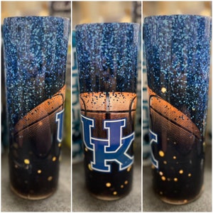 May include: A blue and black tumbler with a basketball and the letters "UK" in blue with white outlines. The tumbler is covered in blue glitter.