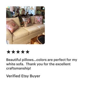 May include: A cream-coloured sofa with four decorative throw cushions. The cushions feature floral patterns in shades of pink, green, and grey. The sofa is in a well-lit room with other decorative items.