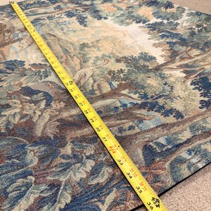 May include: A tapestry with a forest scene in shades of blue, green, and brown. A yellow measuring tape shows the length of the tapestry is approximately 38 inches. The tapestry has a detailed woven design.