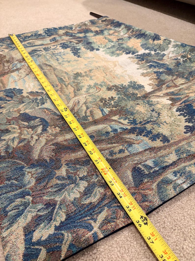 May include: A tapestry with a forest scene in shades of blue, green, and brown. A yellow measuring tape shows the length of the tapestry is approximately 38 inches. The tapestry has a detailed woven design.
