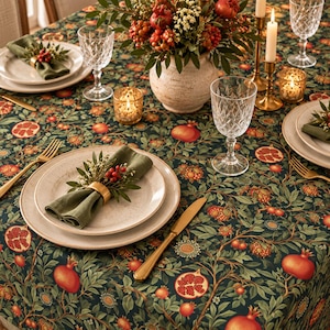 Könnte beinhalten: Eine dunkelgrüne Tischdecke mit einem sich wiederholenden Granatapfel- und Blattmuster, gedeckt mit gesprenkelten Keramiktellern, olivgrünen Servietten in goldenen Ringen, Kristallgläsern, goldenem Besteck und einem floralen Granatapfel-Mittelstück.