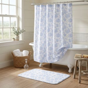 May include: A blue and white floral patterned shower curtain in a bathroom. A matching bath mat is on the floor. A wicker basket holds white towels. A white clawfoot tub is in the background.
