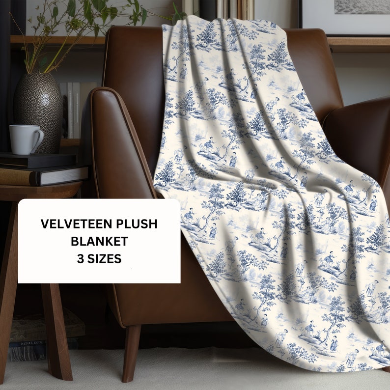 May include: A velveteen plush blanket featuring a blue and white toile pattern with detailed illustrations of figures and trees. A white rectangular overlay on the blanket displays the black text: VELVETEEN PLUSH BLANKET 3 SIZES.
