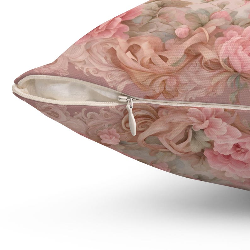 May include: A cushion with a floral design in pink, peach, and cream tones. The pattern includes roses and elaborate scrollwork. A white zip is visible along the edge of the cushion.